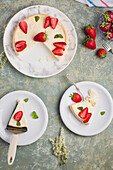 Draufsicht auf Scheiben eines leckeren süßen gebackenen Käsekuchens mit reifen Erdbeeren, serviert auf weißen Tellern auf einem Tisch in einer hellen Küche