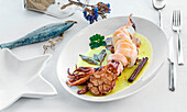Top view of a still life with a fresh tasty served squid on white plate dish with garlic laurel and cinnamon stick with oil on a table set with cutlery and decorated with a glass jar with sand and dried flowers and a bait in the shape of a fish
