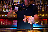 Young Asian bartender pouring gin in jigger while preparing a gin tonic cocktail in the bar