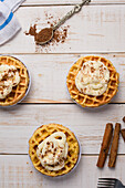 Top view of fresh baked homemade pumpkin cheese waffles with frosting placed on wooden table with cinnamon sticks in light kitchen