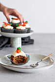 Halb gegessener Karotten-Cupcake mit Sahne auf einem Teller vor einer unscharfen Person, die sich um das Dessert kümmert
