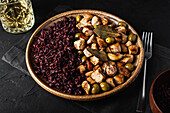 From above of round plate with tasty sauteed turkey with olives placed near glass of beverage on black table in restaurant