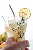 Crop unrecognizable person with glass of refreshing nonalcoholic pear cocktail with lemon slice and rosemary sprig