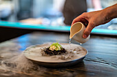 Anonymer Mann gießt flüssigen Stickstoff aus einer Sauciere auf einen Teller mit Seeigel in einem Restaurant mit Molekularküche