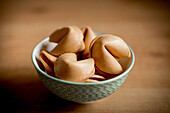 Closeup small bowl full of crispy fortune cookies placed on wooden table