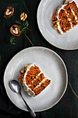 Top view of yummy cake with cream cheese served on plates with fresh carrot slices and walnuts