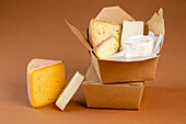 Umweltfreundliche Papierschachteln mit verschiedenen Käsesorten auf braunem Hintergrund gestapelt