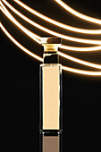 Composition of stylish perfume bottle with golden lid placed on black background near luminous illumination