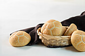 Leckere, frisch gebackene Brötchen in einer Weidenschüssel neben braunem Stoff vor weißem Hintergrund