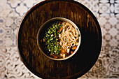 From above ceramic bowl with Chinese ramen meal on circle wooden tray on oriental ornament background