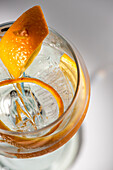 Draufsicht auf ein transparentes Glas mit einem Highball-Cocktail, dekoriert mit Zitrusfruchtschalen und Nelken im Schatten des Sonnenlichts