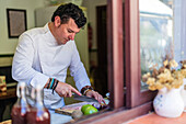 Fokussierter männlicher Koch in Uniform schneidet Fischfilet auf einem Brett, während er am Tisch mit verschiedenen Zutaten in der Küche steht