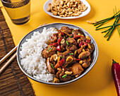From above composition bowl with kung pao chicken with white rice peanut and red hot chili pepper and green onion and chopsticks