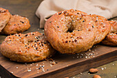 Tasty baked low carbohydrate bagels on wooden cutting board placed on table with almonds in light kitchen
