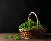 Weidenkorb mit grünen Blättern von frischem Salat auf dem Tisch auf schwarzem Hintergrund
