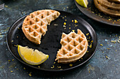 Halves of round tasty homemade baked sweet cheese waffles served on black plate with sour lemon and zest in light kitchen