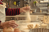 Seitenansicht eines anonymen älteren Kochs, der den Tisch mit Mehl bestreut, nachdem er eine Teigkruste für eine Quiche zu Hause vorbereitet hat