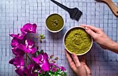 Top view composition with crop anonymous female master with bowl of died powdered henna near brush wooden comb and burning candles for natural hair care