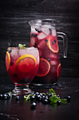 Glass and jug with refreshing cold lemonade with fresh blueberries and lemon slices placed on dark table