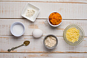 Draufsicht auf verschiedene ungekochte Zutaten für Kürbisfrikadellen mit geriebenem Käse und Mehl neben dem Ei auf einem Holztisch in der Küche