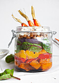Salat mit bunten, reifen, gehackten Paprikaschoten und Bulgur mit rohen Karotten in einem Glas auf einem Tisch vor weißem Hintergrund