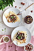 Draufsicht auf leckere Crêpes, die mit Schokolade und Nüssen garniert auf einem Teller auf dem Frühstückstisch serviert werden