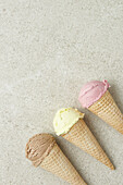 Top view of appetizing chocolate vanilla and berry ice creams in crispy waffle cones placed in row on marble surface