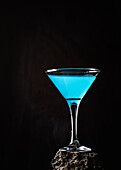 Blue Lagoon cocktail in crystal elegant glass placed on rough surface against black background