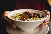 Closeup bowl of delectable Asian noodle soup with pork ribs placed on cafe table