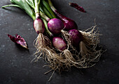 From above of fresh ripe purple onions with green stems placed on black table