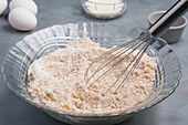 Blick von oben auf eine Glasschüssel mit gemischten trockenen Zutaten für Muffinteig mit rostfreiem Schneebesen während der Zubereitung in der Küche