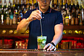 Unrecognizable bartender holding the glass and stirring mojito cocktail in the bar