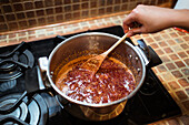 From above of crop anonymous person stirring fig confiture in cooker on stove at home