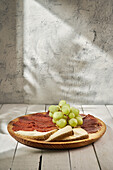 Wooden platter with delicious cheese and sliced wurst garnished with ripe juicy grapes serves on plank table