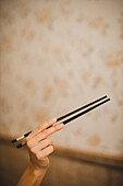 Hand of woman holding traditional Asian bamboo chopsticks on beige mottled background