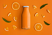 Von oben Flasche frischer Orangensaft auf orangefarbenem Hintergrund mit Orangenscheiben und Orangenbaumblättern