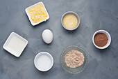 Draufsicht auf verschiedene Zutaten mit Rohrzucker und Butter für hausgemachte Schokoladenwaffeln in einer hellen Küche auf grauem Hintergrund