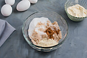 Blick von oben auf eine Glasschale mit verschiedenen Zutaten für gesunde Keto-Kaffee-Muffins mit Zucker und Mehl auf einem grauen Tisch