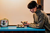Side view of overjoyed Asian woman in sweater sitting at blue table with traditional drink in cafe