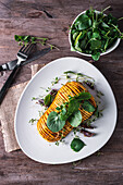 Top view of roasted butternut squash with green leaves of spinach on ceramic plate near cutlery