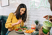 Cheerful female at table with appetizing meal and smoothies against crop anonymous ethnic partner in restaurant