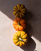 Top view of fresh ripe pumpkins placed on marble beige table in kitchen in sunlight