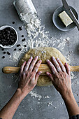 Crop hand of unrecognizable female using wooden tool to roll fresh dough for pastry in cozy kitchen