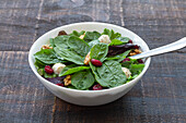 High angle of delicious salad with spinach and beans and walnuts served in bowl on wooden table for healthy lunch