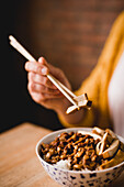 Hands of woman eating with chopsticks from ceramic bowl of yummy Lu Rou Fan dish with tofu placed on table in cafe