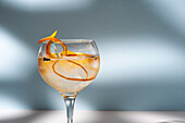 Transparentes Glas mit Highball-Cocktail, verziert mit Zitrusfruchtschalen und Nelken im Schatten des Sonnenlichts
