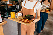Crop girlfriends standing with delicious food and refreshing drinks in cafeteria