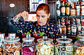 Focused female bartender garnishing fresh cocktails in glasses placed on counter in bar