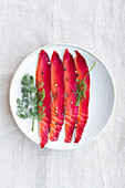 From above gravlax with mixed peppercorns and fresh dill sprigs on plate on light background