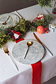 Von oben auf einen weihnachtlich gedeckten Tisch mit Kranzdekoration, rot und weiß, mit goldenem Besteck und Kerzen